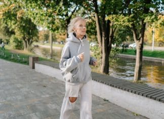 Elderly Woman In Gray Hoodie Sweater Jogging On Pavement