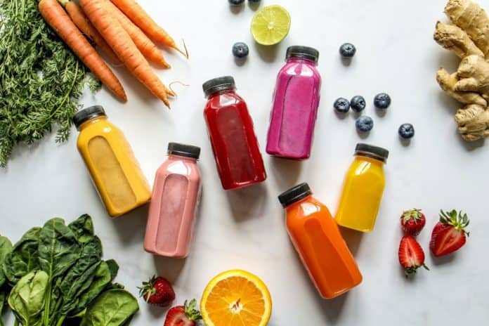 colorful bottles with smoothies beside carrots ginger leaves and berries