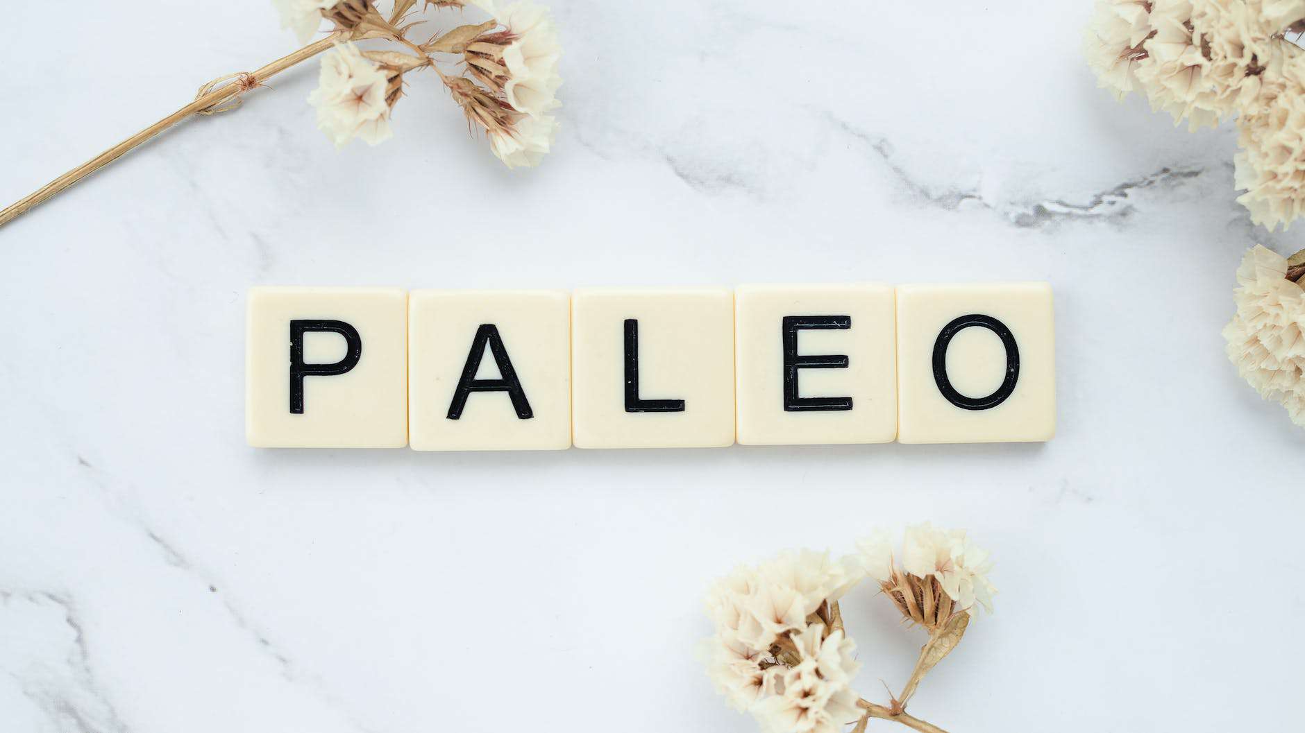 Paleo Letter Tiles Surrounded By White Flowers On A Marbled Surface